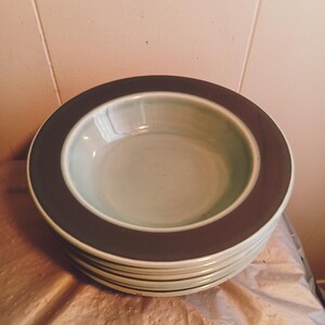 May include: A stack of light green ceramic bowls with a dark brown rim. The bowls are stacked on a brown surface.