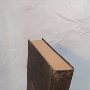 May include: A vintage book with a brown, textured cover and tan-colored pages. The book's spine and edges show signs of wear, suggesting its age. The cover has a decorative embossed design.