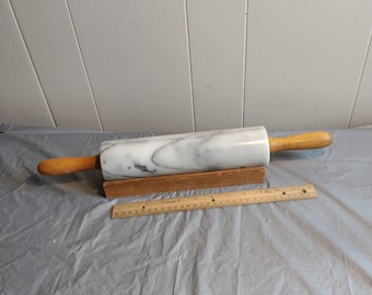 May include: A white marble rolling pin with a wooden handle, resting on a wooden base. The rolling pin is approximately 17 inches long.