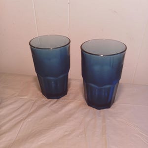 Könnte beinhalten: Zwei blaue Glasbecher mit einem strukturierten Design. Die Gläser sind leer und stehen auf einer weißen Oberfläche.