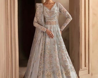 May include: A light blue gown featuring intricate embroidery and embellishments. The gown has a V-neckline, long sleeves, and a flowing skirt. The fabric is sheer and delicate, and the gown is adorned with sequins and beads.