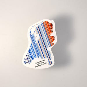 May include: A white sticker in the shape of the Netherlands, featuring climate stripes from 1850-2024. The stripes transition from blue to red, with the text "climate stripes 1850-2024 The Netherlands" in black.
