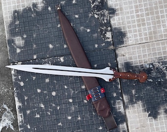 May include: A silver and brown sword with a wooden handle and a leather sheath. The sword has a double-edged blade and a decorative hilt. The sheath is brown with red and blue accents.