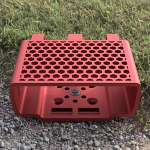 May include: Red plastic case with a honeycomb pattern and a small screw in the center. The case has a rectangular shape with rounded edges.