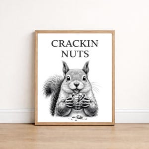 Könnte beinhalten: Gerahmter Schwarz-Weiß-Druck mit einer detaillierten Illustration eines Eichhörnchens, das eine Nuss hält. Der Text "CRACKIN NUTS" ist darüber zu sehen. Das Kunstwerk befindet sich auf weißem Hintergrund.