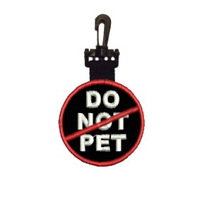 May include: Embroidered patch with the text "DO NOT PET" in white on a black background, crossed out with a red line. It's attached to a black strap and a black plastic clip.
