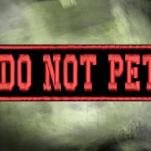 May include: Embroidered patch with the text "DO NOT PET" in red block letters on a black rectangular background. The patch has a red border and is set against a blurred, olive green and gray background.