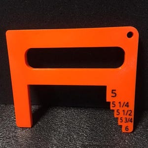 May include: Orange plastic tool with a handle and a series of measurements marked in inches: 5, 5 1/4, 5 1/2, 5 3/4, and 6.