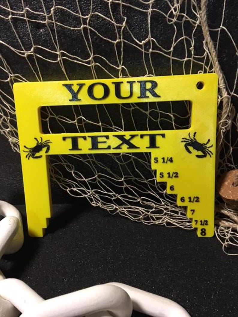 May include: Yellow plastic crab measuring tool with a slot for text. The tool has a scale from 5 1/4 inches to 8 inches. The text "YOUR TEXT" is printed on the tool.