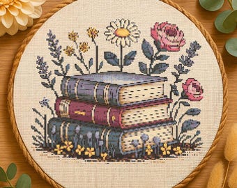 May include: Cross-stitch embroidery in a round wooden hoop. The design features a stack of three books with floral elements, including a daisy, pink roses, and lavender. The color palette includes shades of purple, pink, yellow, and green on a beige background.