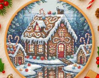 May include: A cross-stitch embroidery of a gingerbread house scene, set in a snowy winter landscape. The house is brown with white icing and candy cane accents, framed in a wooden hoop. Christmas-themed.