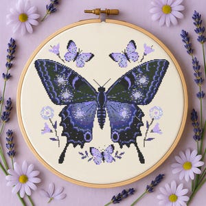 May include: A purple and black butterfly with white accents is embroidered on a white fabric hoop. The hoop is surrounded by lavender flowers and leaves.