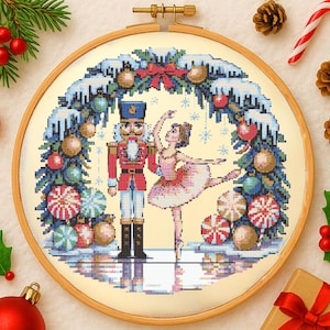 Peut inclure: Broderie au point de croix dans un cercle en bois représentant une scène de Noël avec un casse-noisette et une ballerine. Le motif présente un casse-noisette rouge et blanc, une ballerine en tutu rose et des ornements festifs.