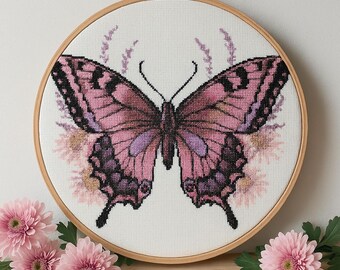 Peut inclure: Une broderie au point de croix représentant un papillon rose et noir dans un cercle en bois. Le papillon est entouré de motifs floraux délicats.