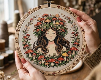 May include: A cross-stitch embroidery in a wooden hoop. The artwork depicts a woman with closed eyes, adorned with a mushroom crown and surrounded by mushrooms and foliage. The hoop is decorated with mushroom and leaf designs.