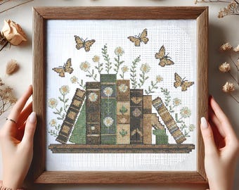 Peut inclure: Un motif de point de croix représentant une pile de livres avec une étagère en bois brun et un motif floral avec des papillons. Les livres sont verts, bruns et beiges avec des accents blancs.