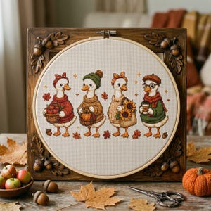 Peut inclure: Une broderie au point de croix représentant quatre canards blancs vêtus de vêtements d'automne, encadrés dans un cadre en bois carré avec des détails sculptés de glands et de feuilles de chêne. Les canards portent des bonnets, des écharpes et des pulls.