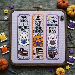 May include: A square wooden embroidery hoop containing three vertical cross-stitch bookmarks on light purple fabric. The designs feature ghosts, a pumpkin, books, and text reading Sorry I Ghosted You, Just One More Chapter, and Reading Is My Boo.