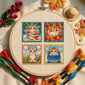 Peut inclure: Un cercle de broderie au point de croix avec quatre motifs carrés de chats roux et blancs dans des décors saisonniers. La broderie est sur un tissu beige, avec du fil à broder coloré et des éléments décoratifs.