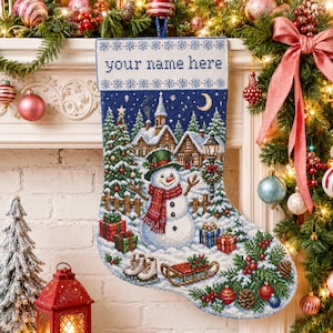 Könnte beinhalten: Ein blauer Weihnachtsstrumpf mit einer im Kreuzstich gearbeiteten winterlichen Dorfszene, einem Schneemann mit grünem Hut und rotem Schal, einer Mondsichel sowie einem weißen Umschlag mit dem Text your name here und Schneeflocken.