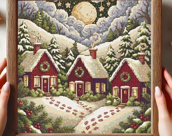 May include: A framed cross-stitch depicting a winter scene with three red houses, snow-covered roofs, and wreaths on the doors. The artwork features a full moon, snowy hills, and evergreen trees. The frame is made of wood.