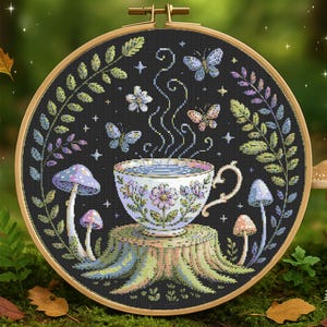 Puede incluir: Un bordado de punto de cruz en un aro de madera presenta una taza de té con vapor, rodeada de mariposas, setas y follaje. La taza está sobre un tocón de árbol, con un fondo oscuro. La paleta de colores incluye azules, verdes y morados.