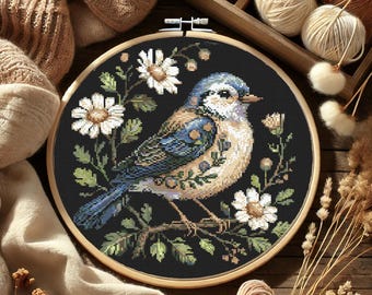 May include: A bluebird with white and brown markings sits on a branch with white flowers. The bird is surrounded by green leaves and is set against a black background. The image is framed in a wooden hoop.