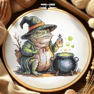 May include: Cross-stitch embroidery of a frog dressed as a wizard, wearing a hat and holding a potion bottle. The frog is next to a bubbling cauldron. The embroidery is set in a wooden hoop.
