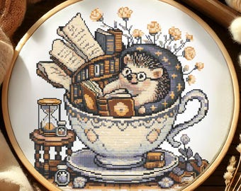 May include: Cross-stitch embroidery in a wooden hoop features a hedgehog wearing glasses and a hat, reading books inside a teacup. The teacup sits on a saucer with more books. An hourglass and small table are on the left.