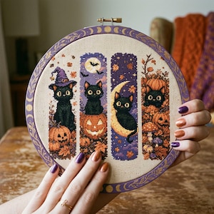 Peut inclure: Un tambour à broder circulaire contenant un motif au point de croix composé de quatre panneaux verticaux illustrant des chats noirs, des citrouilles, des feuilles d'automne et des lunes. Le cadre en bois est peint en violet avec des motifs dorés.