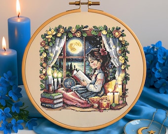 May include: A cross-stitch embroidery hoop with a colorful design of a girl reading a book by a window with a full moon outside. The girl is wearing a blue and white dress and has brown hair. There are candles and flowers around the window.