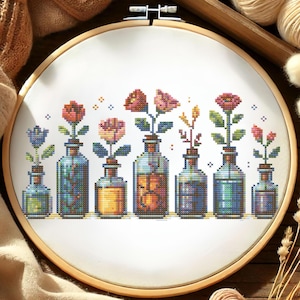 May include: Cross-stitch embroidery of colorful flowers in glass bottles. The design features a variety of blooms in shades of red, pink, and blue, each in a different bottle. The embroidery is set in a wooden hoop.