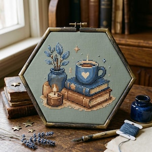 May include: Hexagon-shaped cross-stitch art featuring a cozy scene. A blue mug with a heart sits atop books, next to a vase with blue leaves and a lit candle. The frame is a dark bronze color.