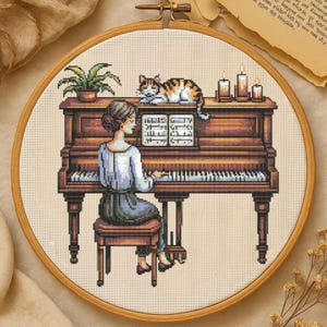 May include: Cross-stitch embroidery of a woman playing a grand piano. A calico cat rests on top of the piano, next to lit candles and a small potted plant. The piano is brown with white keys, and the woman is wearing a blue dress.