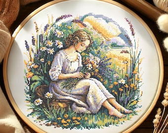 May include: A completed cross-stitch embroidery in a wooden hoop. The artwork depicts a woman in a field of flowers, with a landscape background. The color palette includes greens, yellows, purples, and whites. The embroidery is framed in a round wooden hoop.