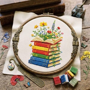 May include: A cross-stitch embroidery hoop featuring a stack of colorful books with flowers and butterflies. The books are in shades of blue, red, yellow, and green. The embroidery hoop is made of wood and has decorative metal accents.