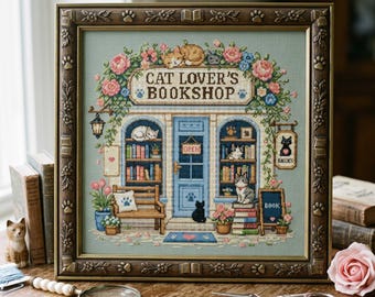 May include: A framed cross-stitch embroidery depicting a storefront titled Cat Lover's Bookshop. The scene features a blue door, bookshelves filled with books, various cats, and floral accents in pink, blue, and green, all encased in a brown frame.