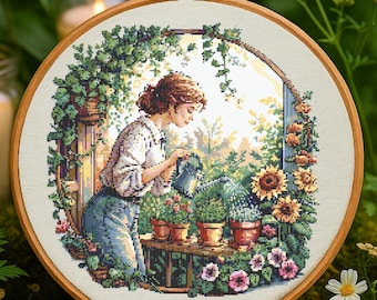 May include: A cross-stitch embroidery of a woman watering plants in a garden setting. The woman is wearing a white shirt and blue jeans. The garden is filled with flowers and greenery. The embroidery is framed in a wooden hoop.