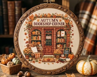 May include: A circular embroidery hoop frame containing a cross-stitch design of a storefront labeled "AUTUMN BOOKSHOP CORNER." The scene features bookshelves, a cozy chair, pumpkins, and fall foliage in shades of orange, brown, and green.
