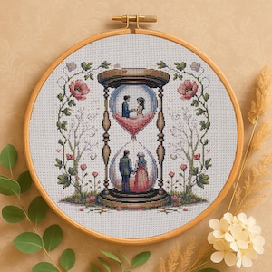 Può includere: Ricamo a punto croce in un telaio di legno. Il disegno presenta una clessidra con due coppie all'interno, una in alto e una in basso. Rose rosa e viti verdi incorniciano la clessidra. Lo sfondo è beige chiaro.