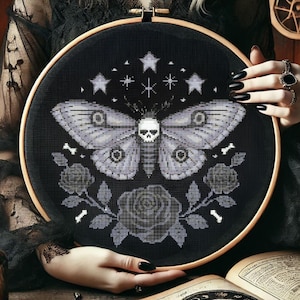 May include: Black and white embroidery hoop with a moth with a skull head, surrounded by roses and bones. The moth has a gray and white pattern on its wings. There are five stars above the moth.