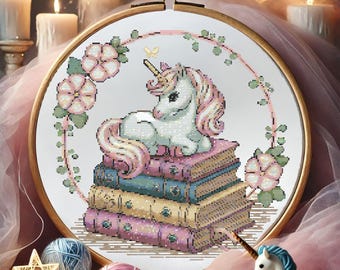 Puede incluir: Un unicornio blanco con una melena y cola rosadas se sienta sobre una pila de libros coloridos. El unicornio está rodeado de flores rosas y hojas verdes.