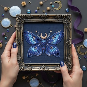 May include: A framed cross-stitch of a blue moth with a crescent moon and star details. The moth is set against a dark blue background within an ornate, antique-style frame. The artwork is surrounded by decorative elements.