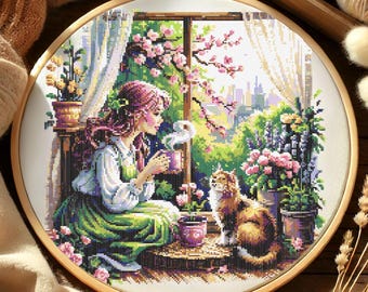 May include: A cross-stitch embroidery hoop featuring a serene scene of a woman enjoying a cup of coffee by a window, with a cat. The scene includes blooming flowers, a cityscape, and a cozy interior. The embroidery is set in a wooden hoop.