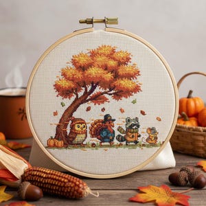 Peut inclure: Une broderie au point de croix dans un cercle en bois représente une scène d'automne. Un grand arbre aux feuilles orange et jaunes abrite un hibou, une dinde, un raton laveur et une souris. Citrouilles, glands et maïs complètent le thème automnal.