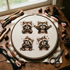 May include: A cross-stitch embroidery hoop featuring four raccoon designs. The raccoons are in various poses, with brown and tan thread used for the details. The hoop is surrounded by embroidery floss, acorns, and scissors on a wooden surface.