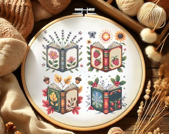 May include: A cross-stitch embroidery hoop featuring four open books, each representing a season. The books are adorned with floral and seasonal motifs, including flowers, strawberries, autumn leaves, and snowflakes. The embroidery is set in a wooden hoop.