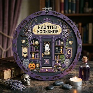 May include: A circular cross-stitch embroidery in a purple wooden frame featuring a haunted bookshop scene. The design includes a ghost, a black cat, a jack-o'-lantern, skulls, and books, with the text HAUNTED BOOKSHOP and OPEN displayed clearly.