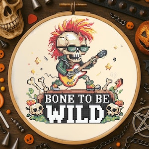 May include: A cross-stitch embroidery in a wooden hoop features a skeleton playing a guitar, wearing sunglasses and a mohawk. The text "BONE TO BE WILD" is displayed below the skeleton. The design is surrounded by Halloween-themed decorations.