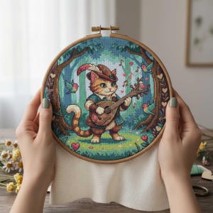 Puede incluir: Bordado de punto de cruz de un gato jengibre tocando un laúd en una escena de bosque. El gato lleva un sombrero con una pluma y una túnica azul. El fondo presenta árboles, pájaros, notas musicales y corazones, todo dentro de un bastidor de madera.